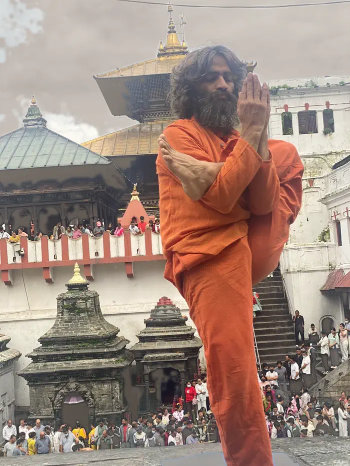 Yogi Ji standing in a balancing posture with hands joined, the gilded roof of Pashupatinath behind him.