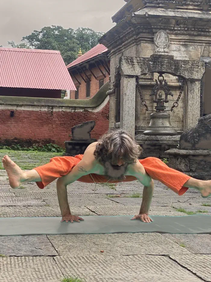 Yogi Ji holding an arm balance, legs extended, on the stone paving before a temple wall.
