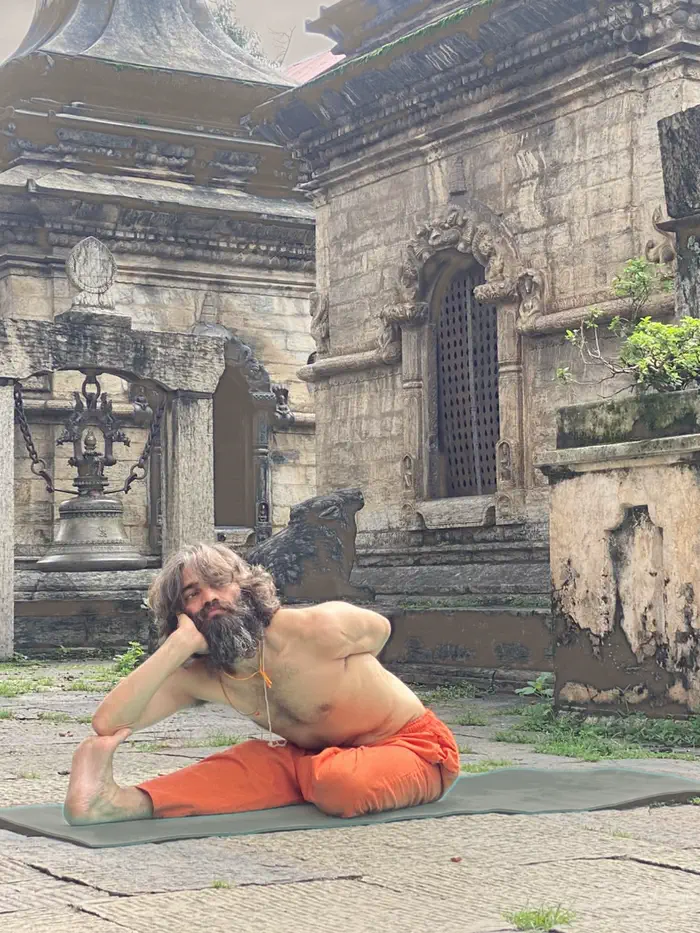 Yogi Ji kneeling forward in a quiet resting posture on his mat in the temple courtyard.