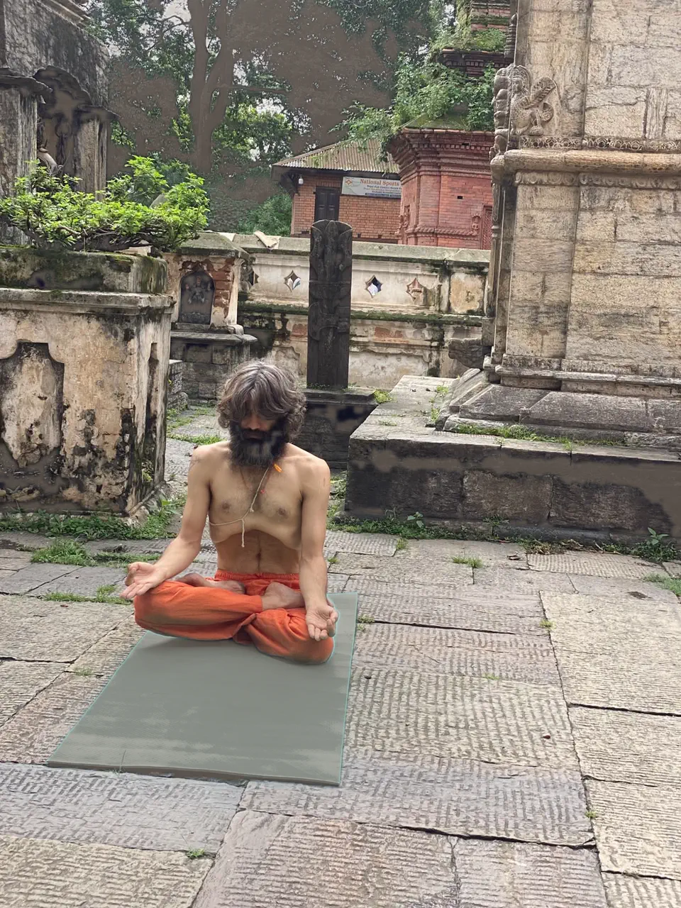 Yogi Ji sitting cross-legged on worn stone among the shrines and lingams of the Pashupatinath temple complex.